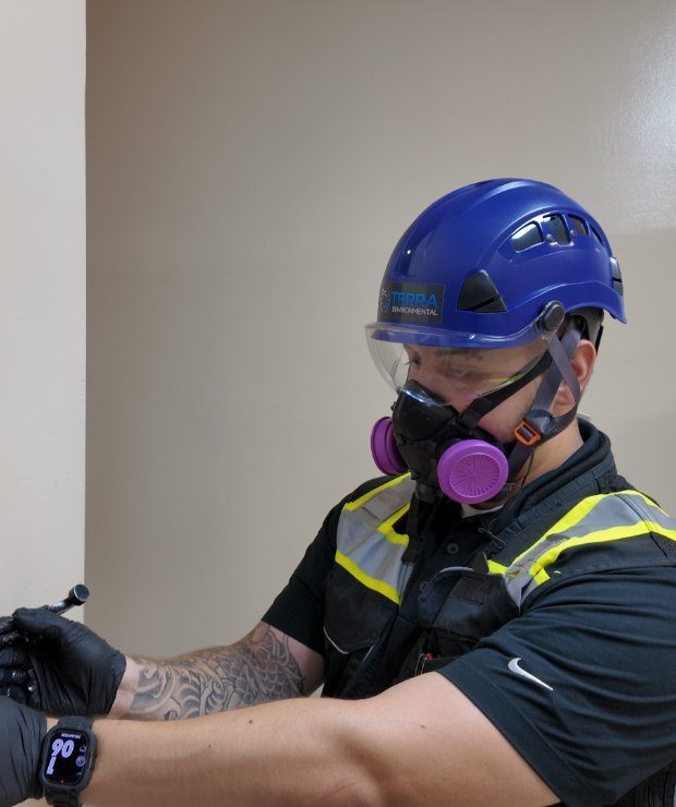 TERRA technician in respirator and hard hat collecting a bulk sample